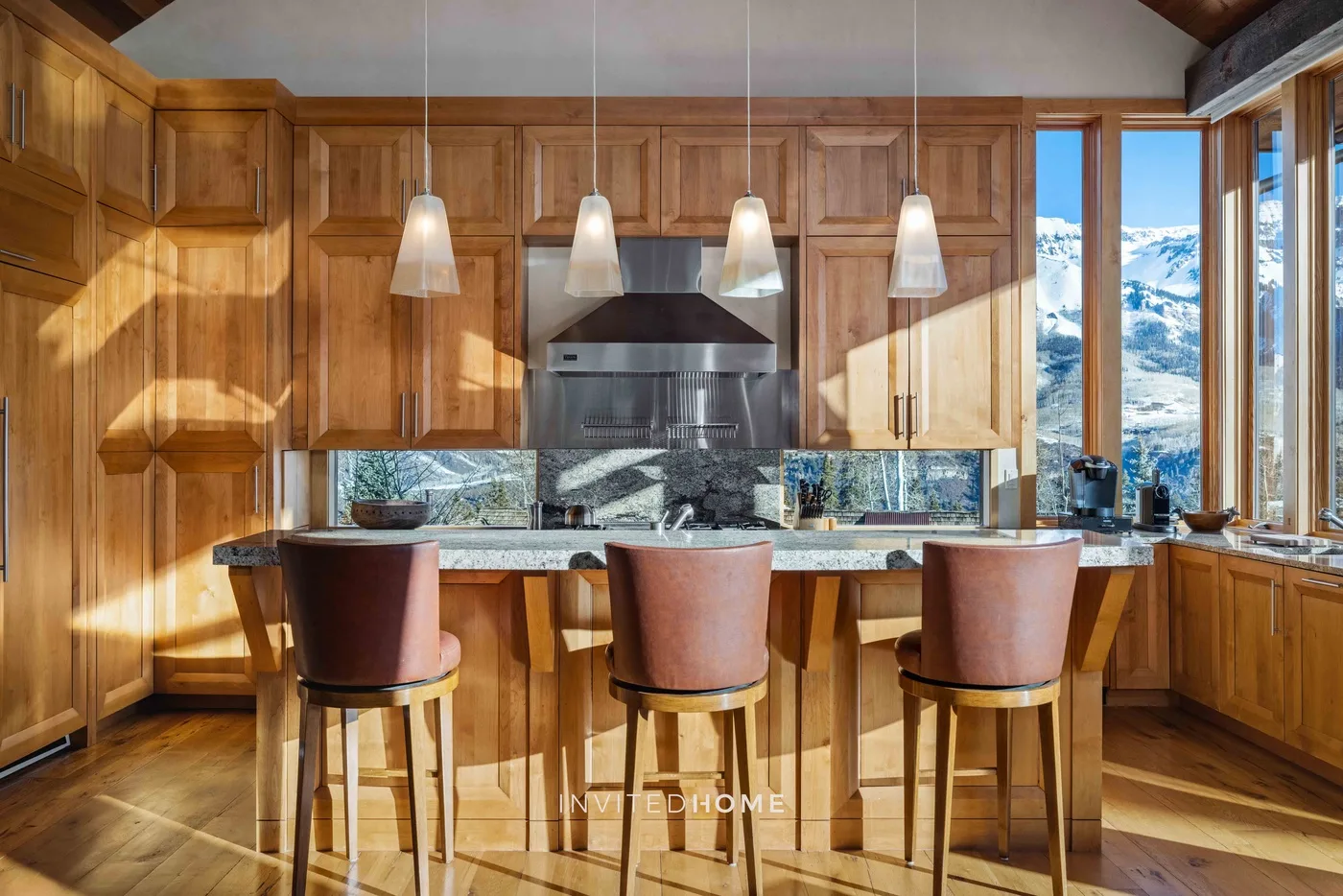 A wood-paneled kitchen with a central island, pendant lights, and large windows.