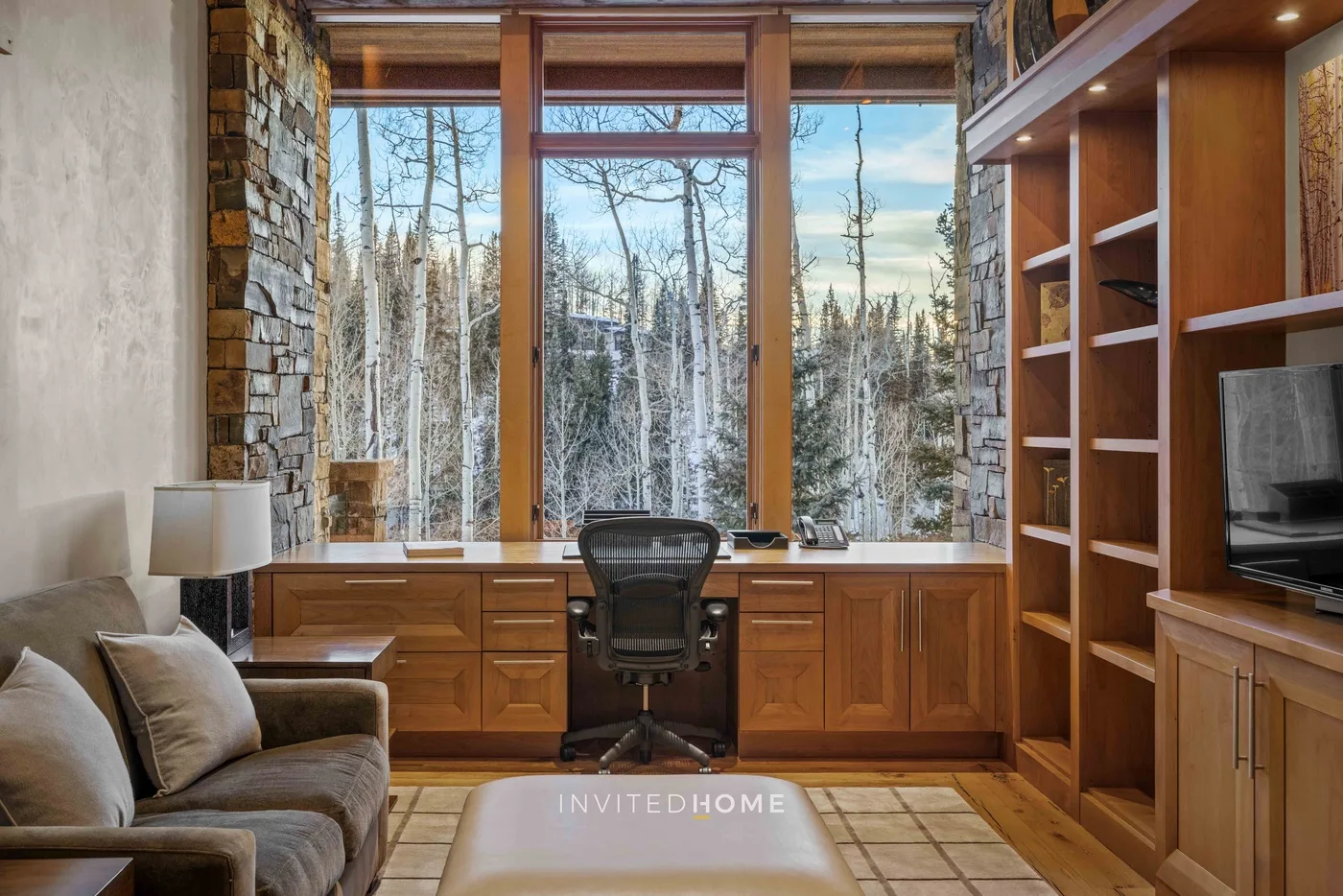 A wood-paneled office with a desk and large windows overlooking trees.