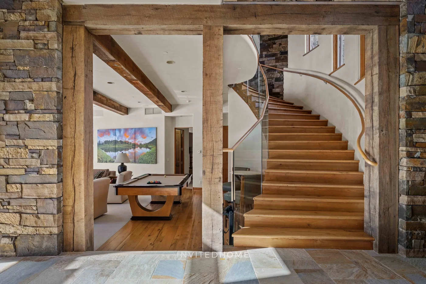 A wooden staircase rises beside a dining area in a rustic interior.