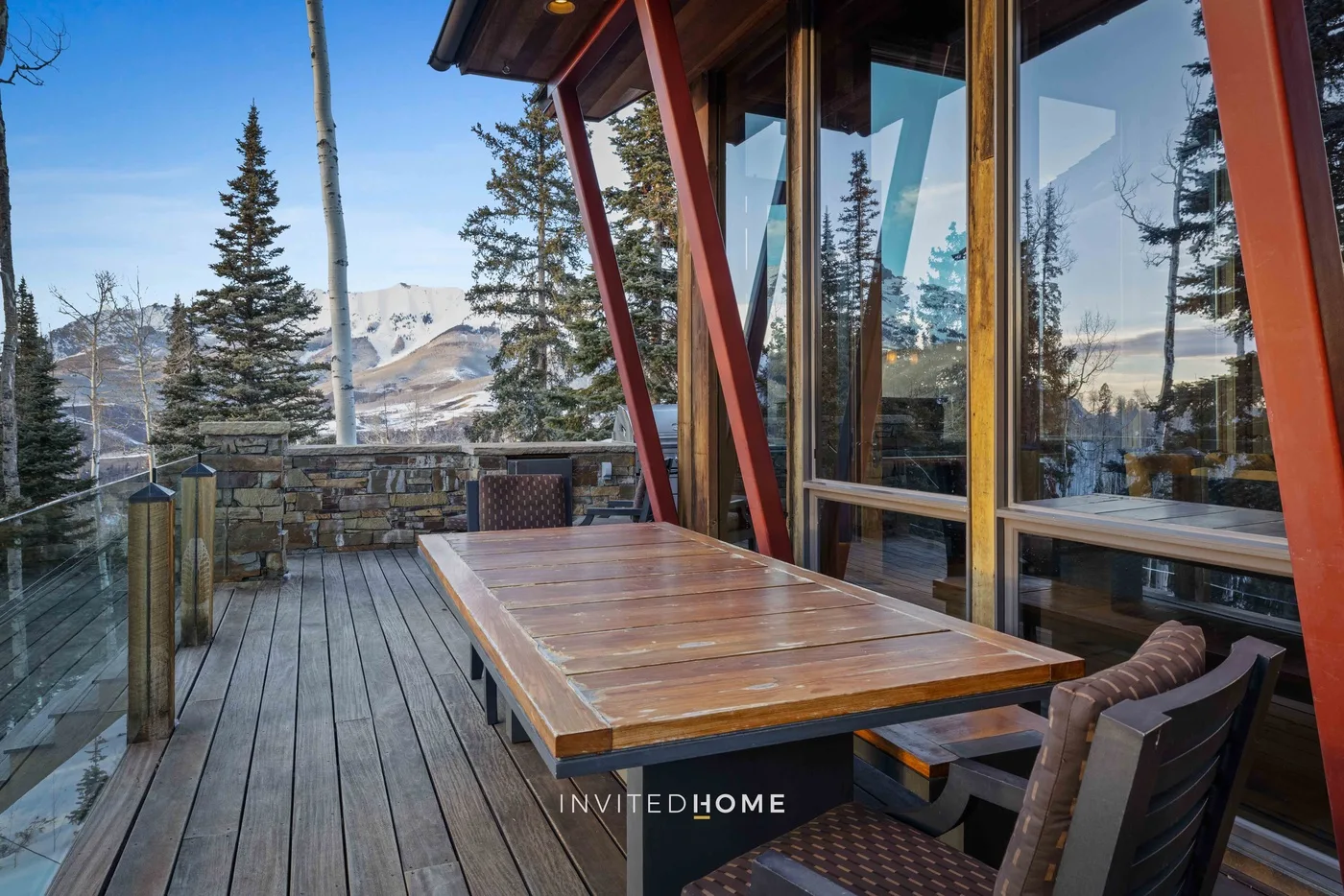 An outdoor deck with a wooden table and chairs overlooks a mountain landscape.