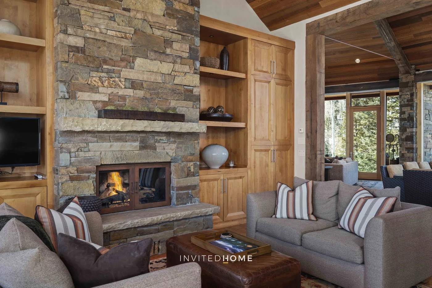 A living room with a stone fireplace, seating, and large windows.