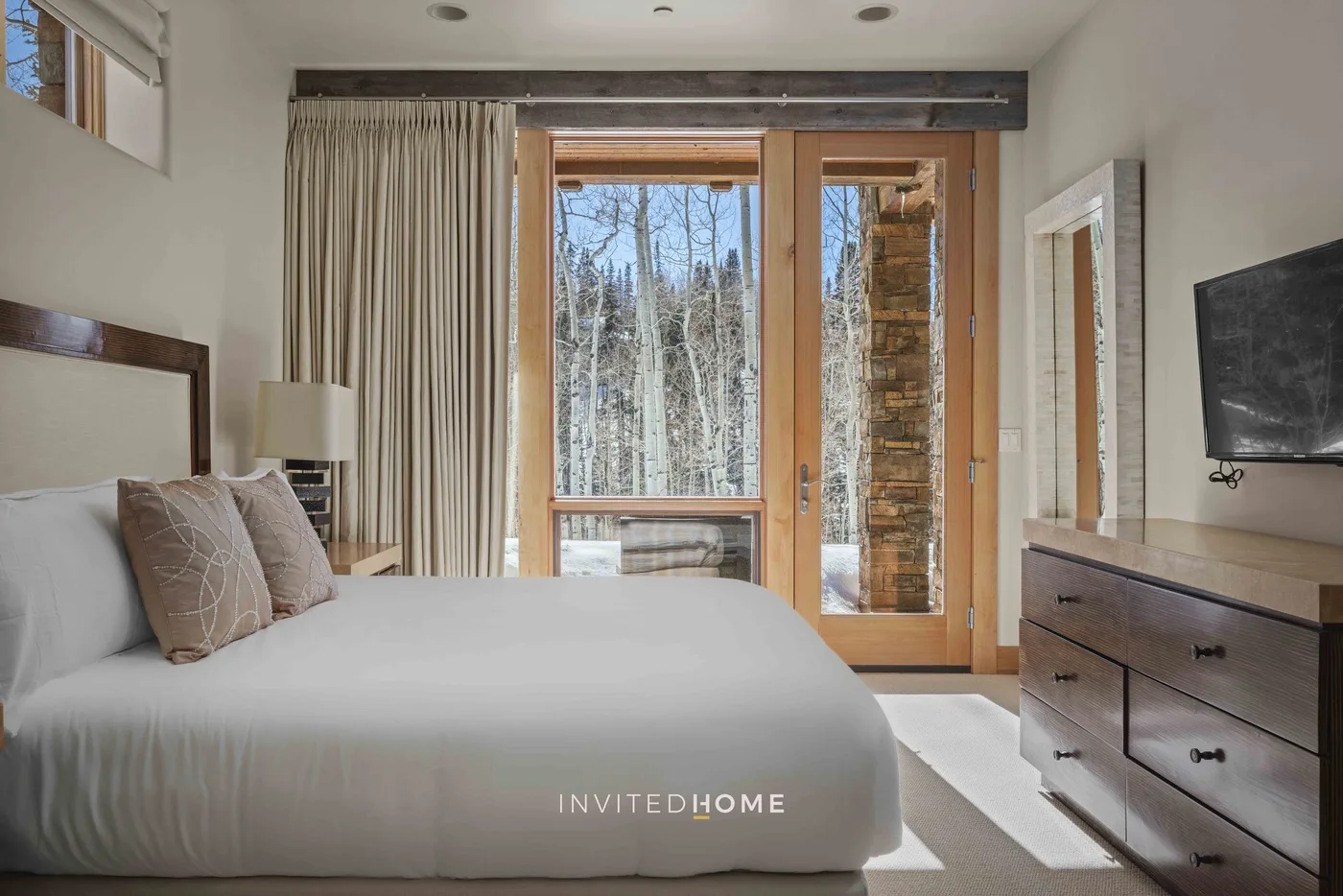 A bedroom with a bed beside tall windows overlooking trees.