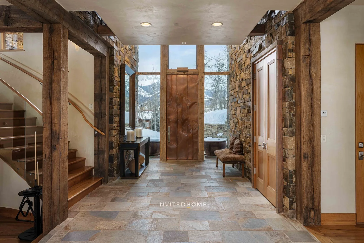 A stone-and-wood entry hall with a staircase and large windows.
