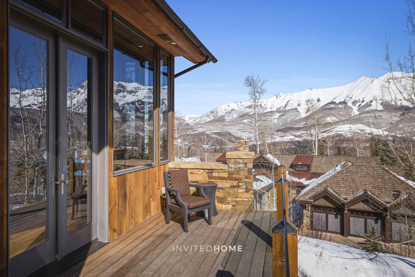 A wooden deck beside a glass-fronted building overlooks snow-covered mountains.