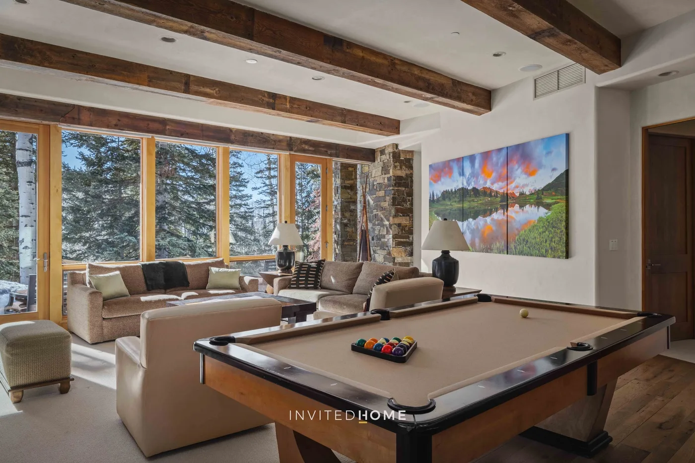 A living room with a pool table, seating, and large windows overlooking trees.