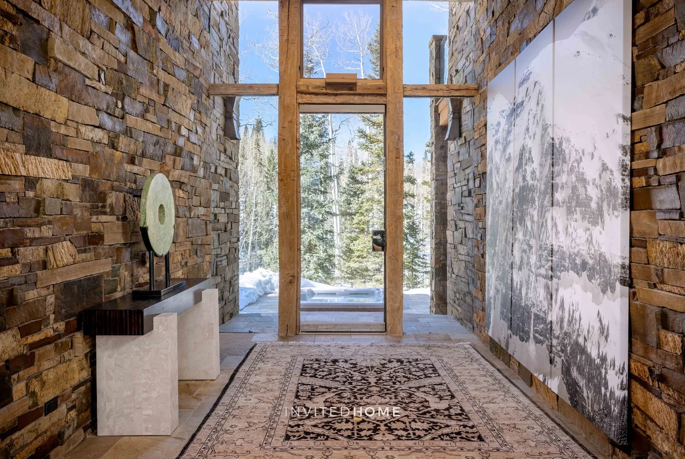 A stone-walled entryway opens to a glass door overlooking snow-covered trees.