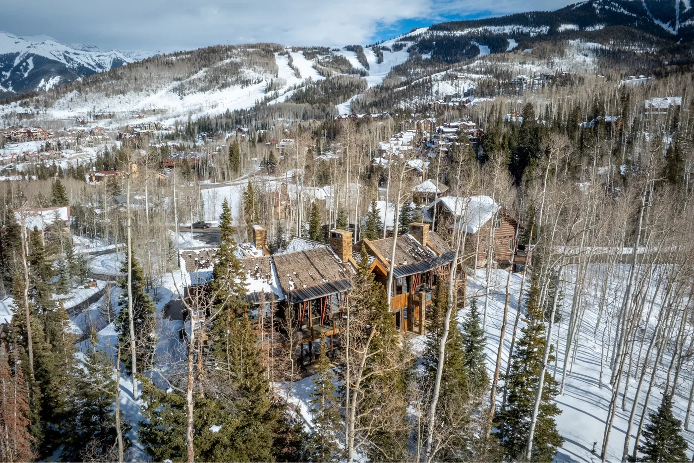 Aerial view of a mountain resort with cabins among snow-covered trees.
