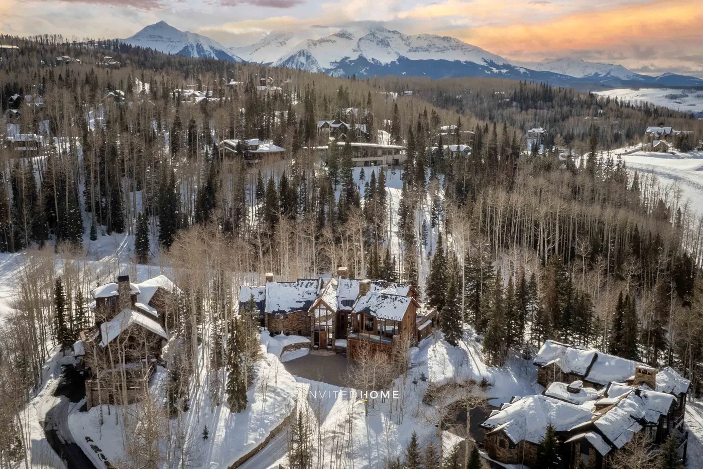 Snow-covered cabins sit among trees, with a mountain range visible in the distance.