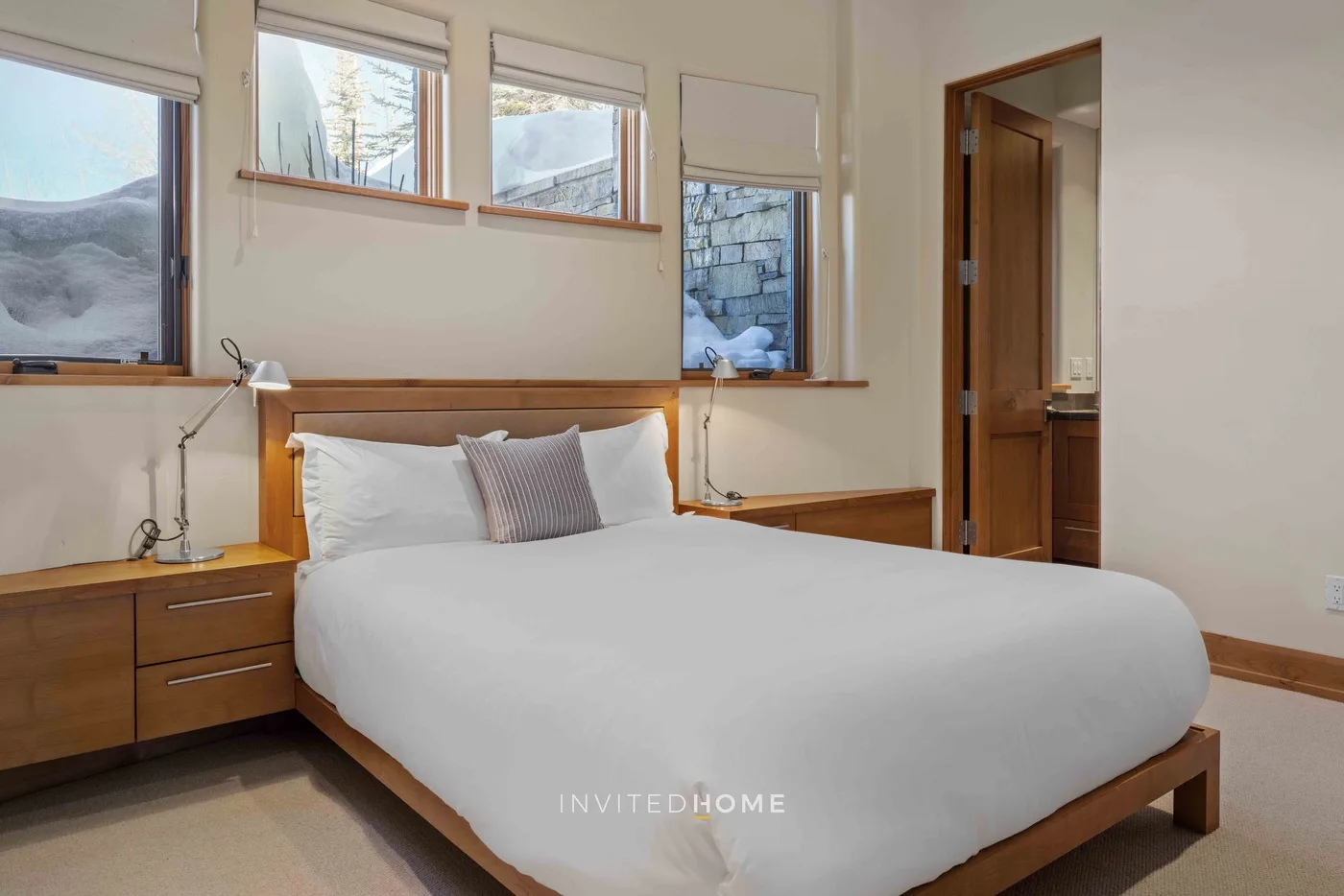 A bedroom with a neatly made bed beneath several windows.