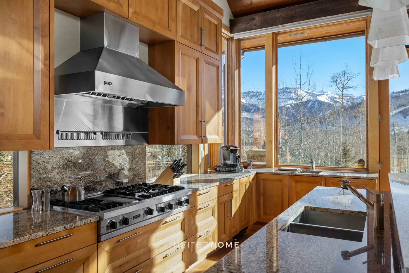 A wood-cabinet kitchen with a large window overlooking a mountain landscape.