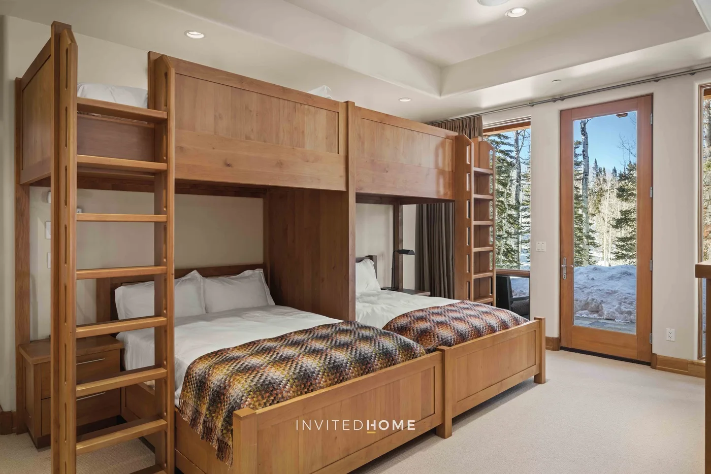 A bedroom with wooden bunk beds and a glass door opening onto a snowy view.