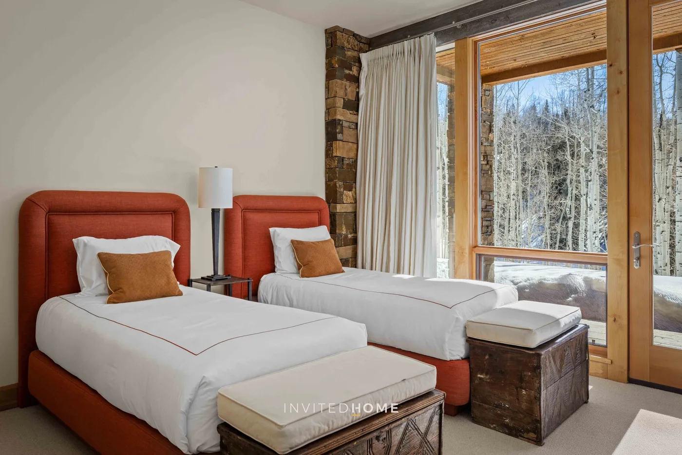 A bedroom with two beds beside a large window overlooking trees.
