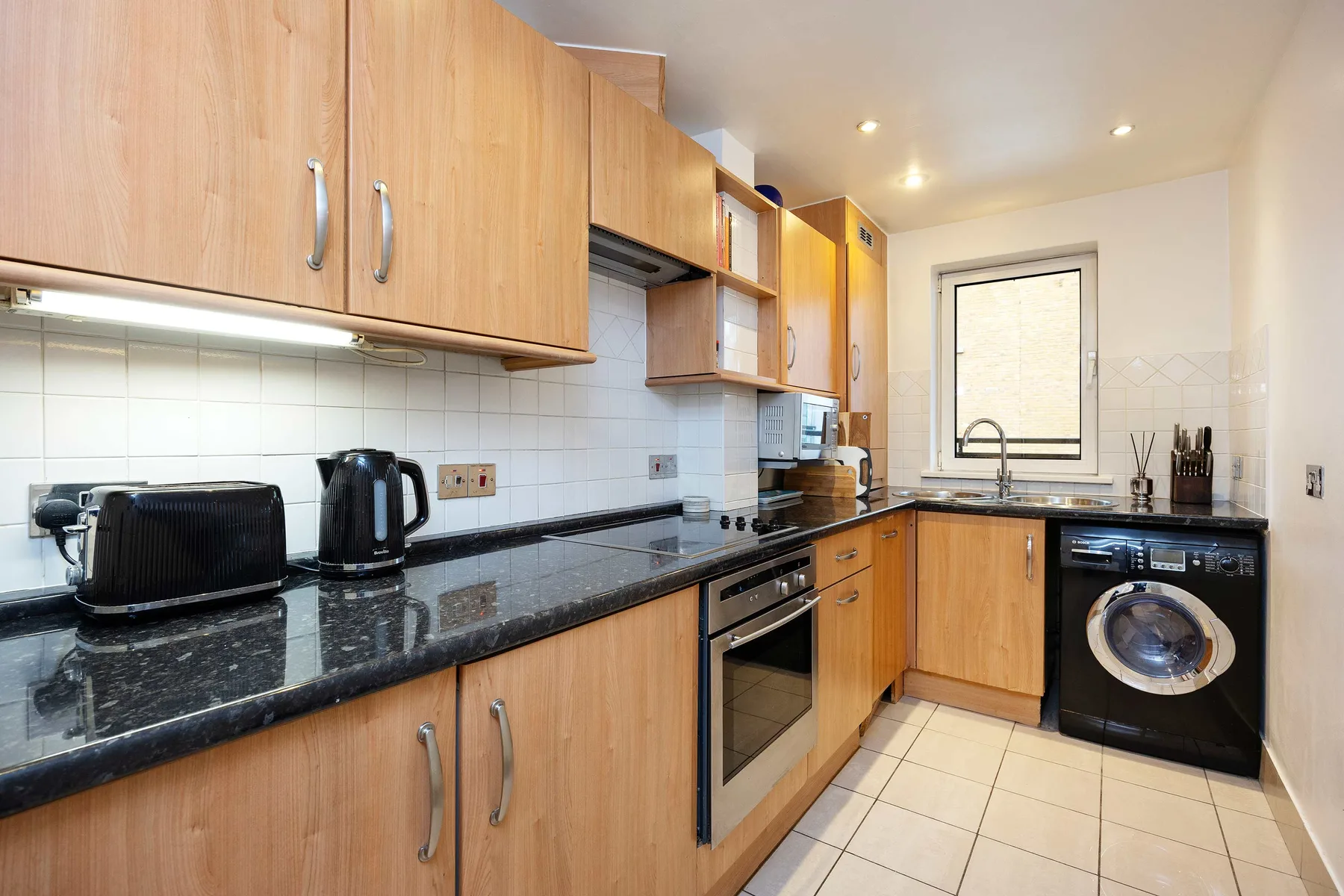 A bright kitchen with wooden cabinets, dark countertops, and a washing machine.