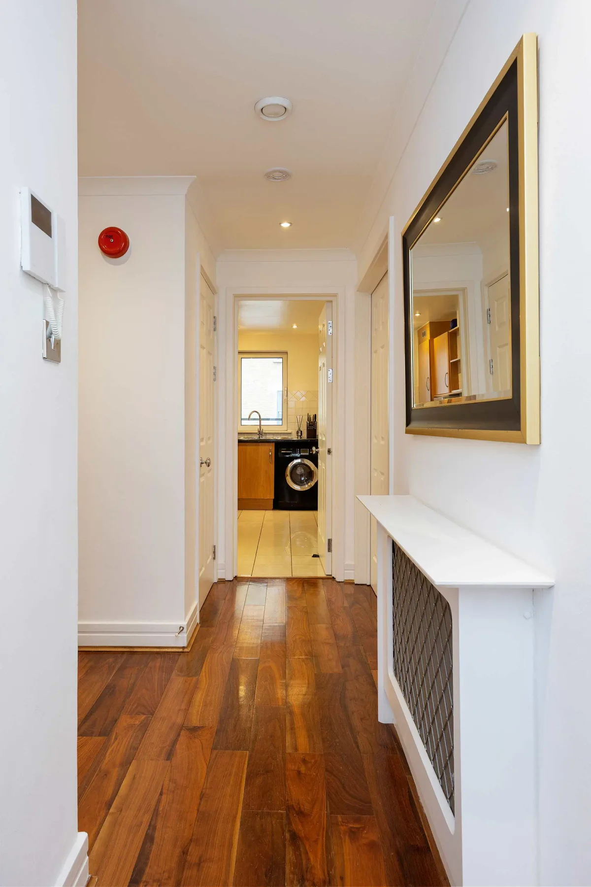 A hallway with wooden flooring leads to a kitchen area.