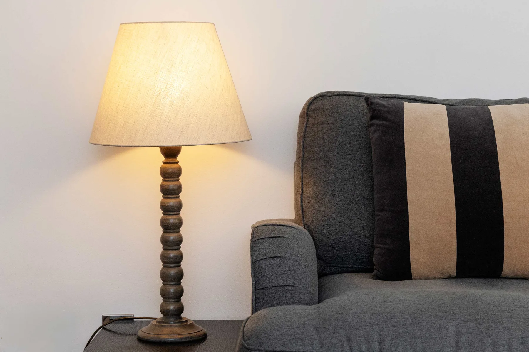 A living room seating area with a dark upholstered seat and a lit table lamp.