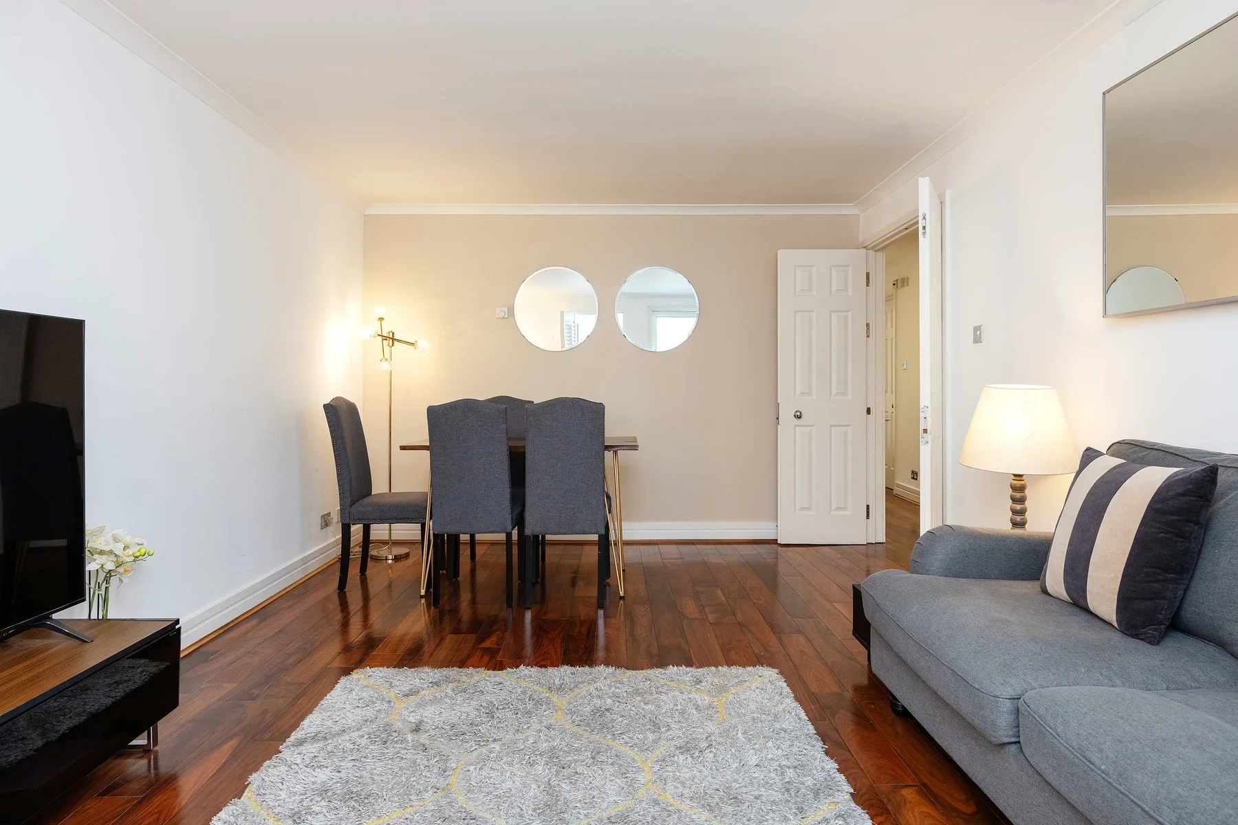 A living and dining area with a gray rug, seating, and a dining table.