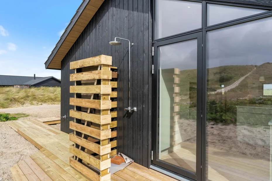 A modern dark-sided cabin with large glass doors and a wooden deck.