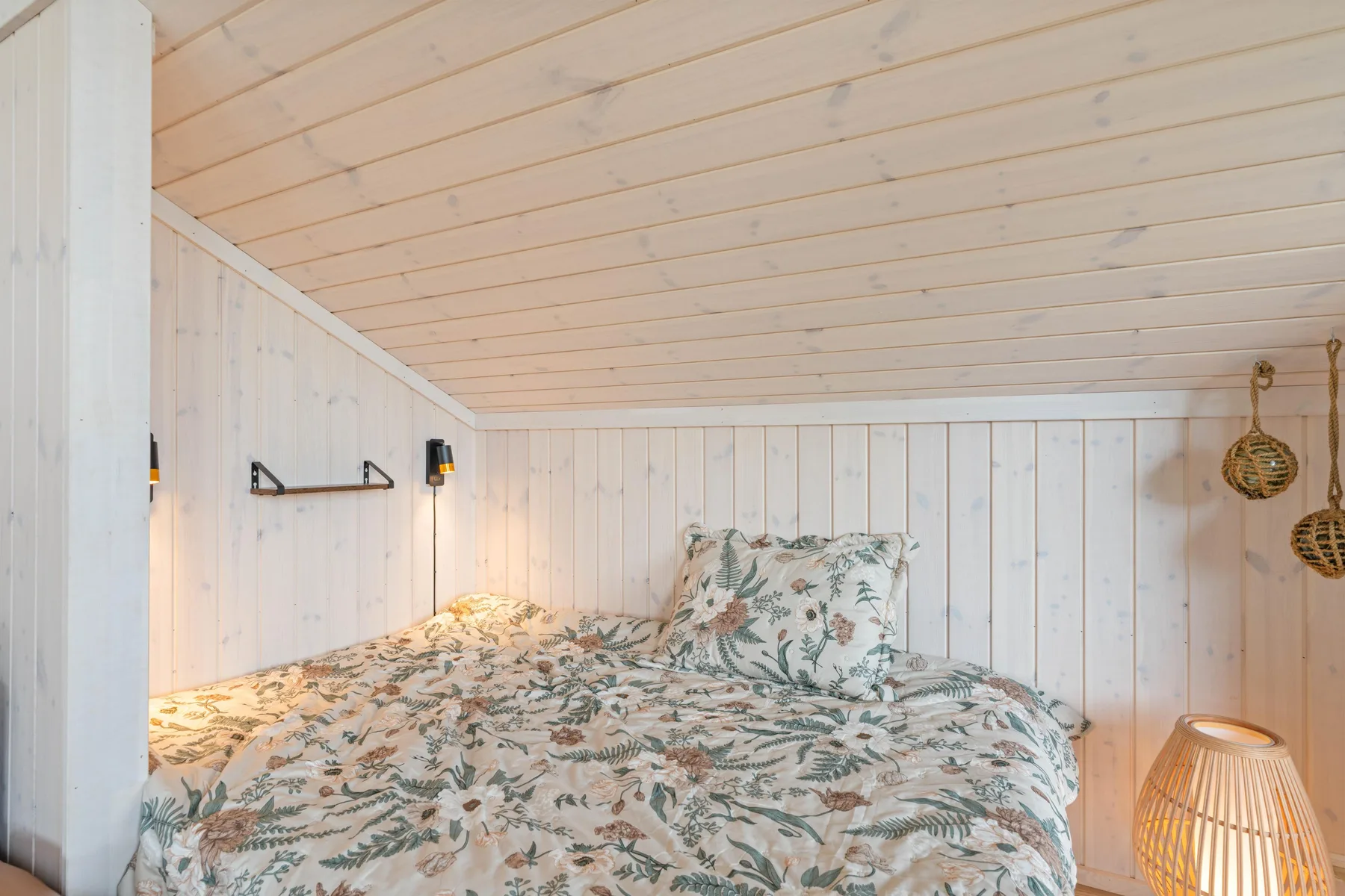 A low-ceiling bedroom with a bed covered in floral bedding.