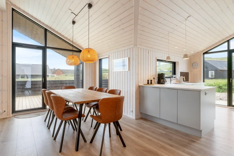 An open dining and kitchen area with a long table beside large windows.