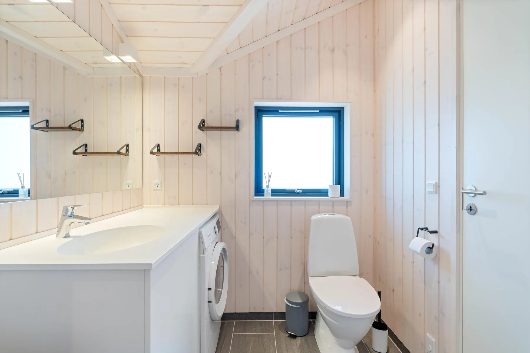 A bright bathroom with a sink, toilet, and small window.