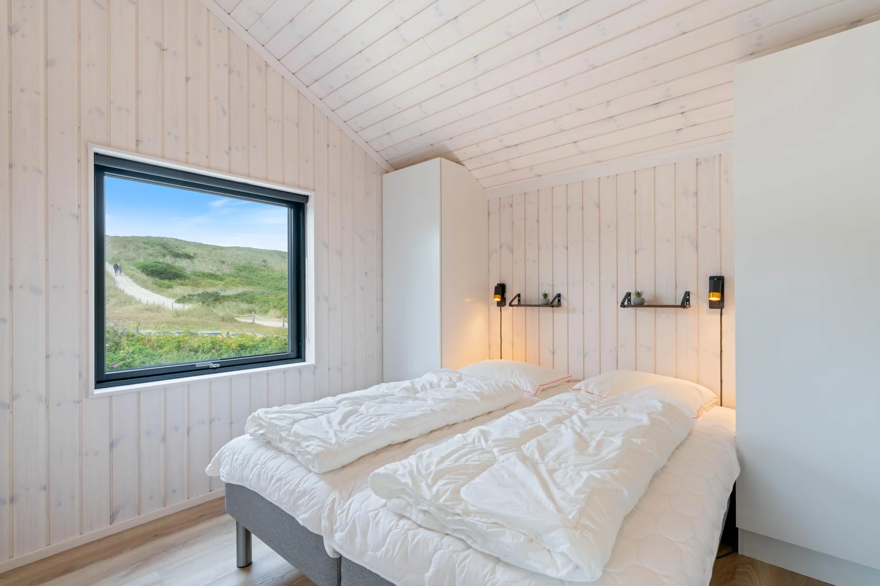 A bedroom with two beds and a window overlooking grassy dunes.