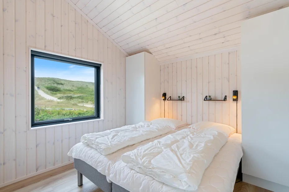 A bright bedroom with two beds beneath a sloped white ceiling.