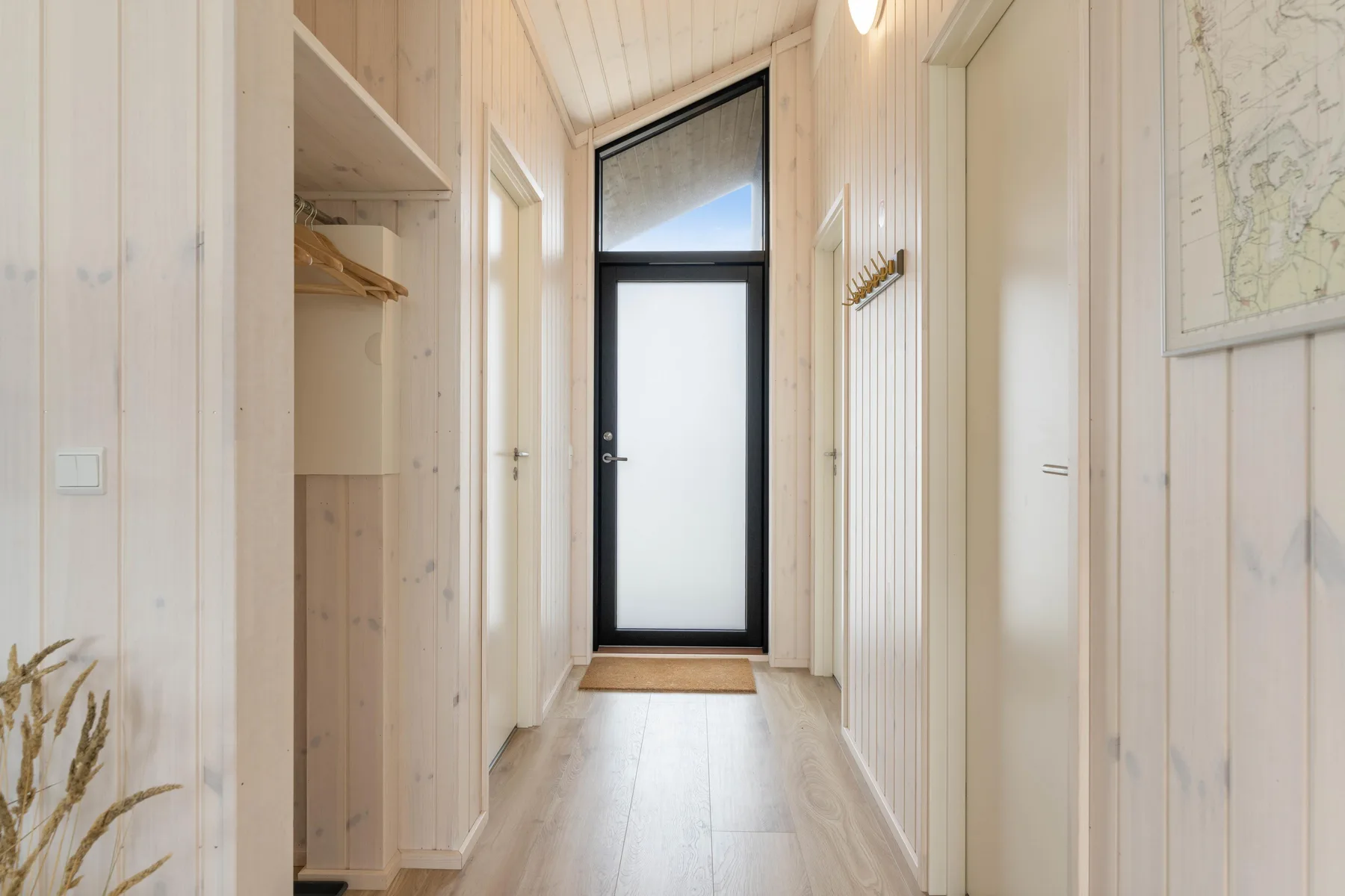 A bright hallway leads to a black-framed entrance door.