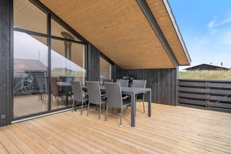 An outdoor dining area on a wooden deck beside large glass doors.
