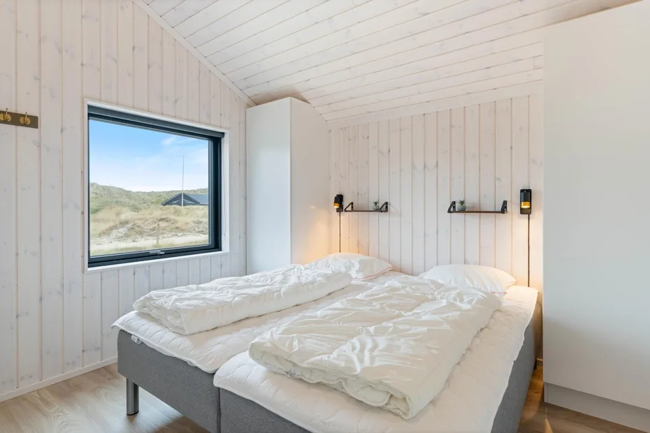 A bright bedroom with two beds and a large window overlooking a grassy landscape.