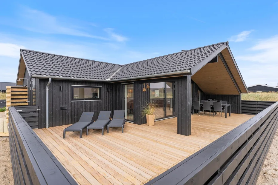A modern house opens onto a spacious wooden deck with outdoor seating.