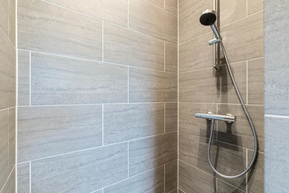 A tiled shower with a handheld showerhead and hose.