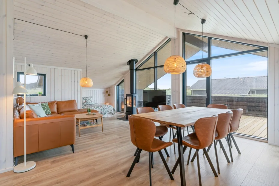 A bright open-plan living and dining area with a wooden table and large windows.
