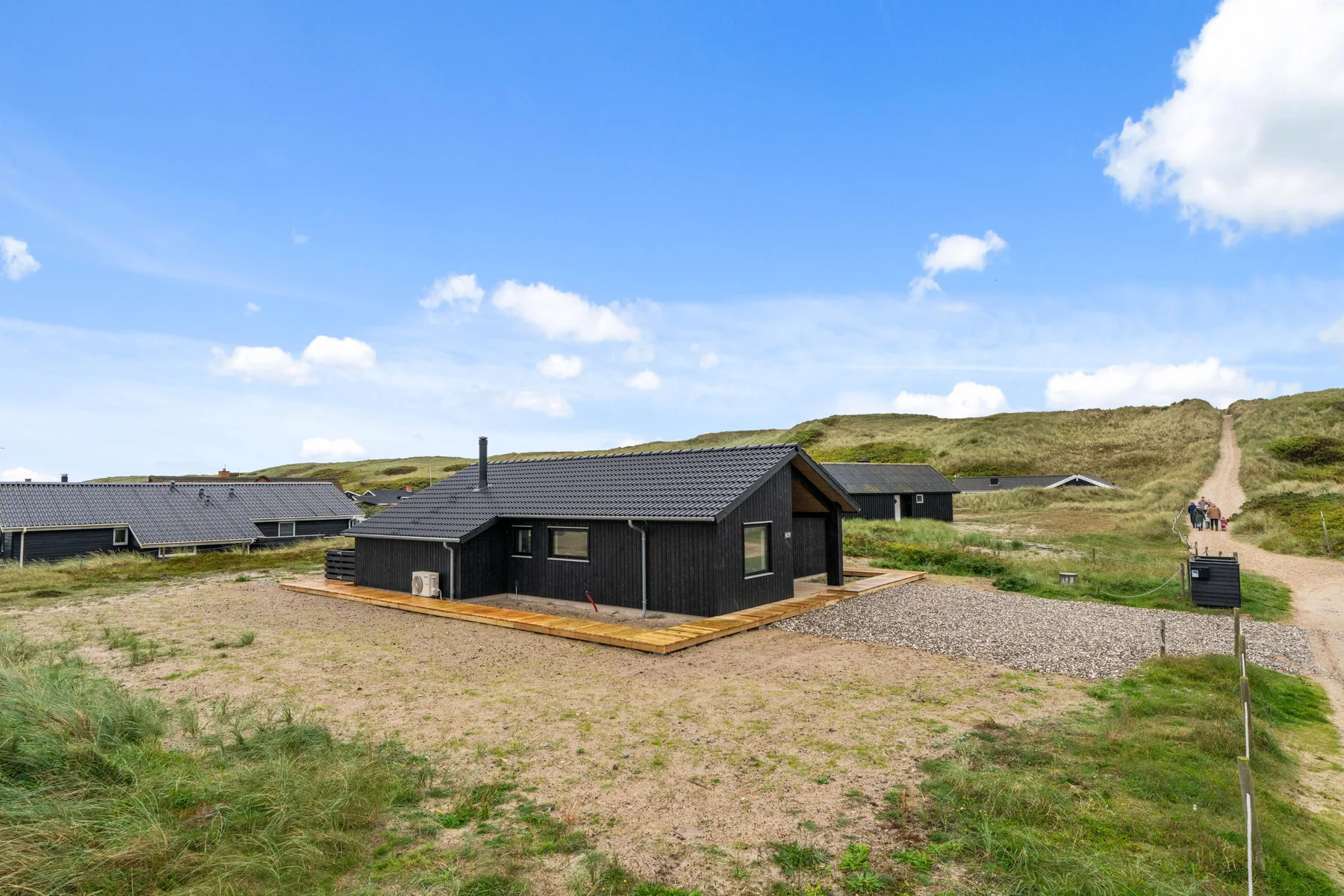 A dark, low building stands in an open grassy landscape beneath a blue sky.