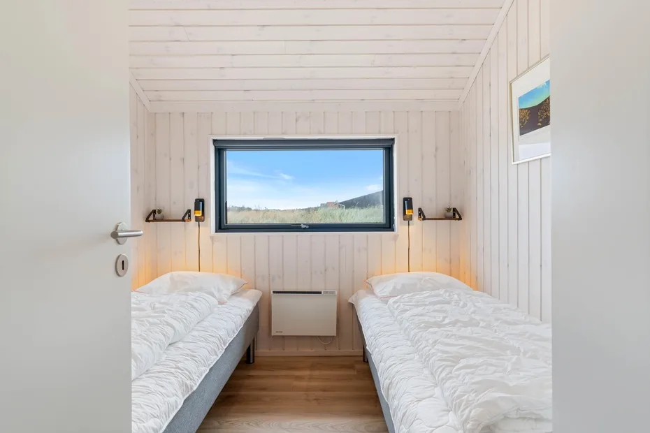 A bright bedroom with two beds facing a wide window overlooking the landscape.