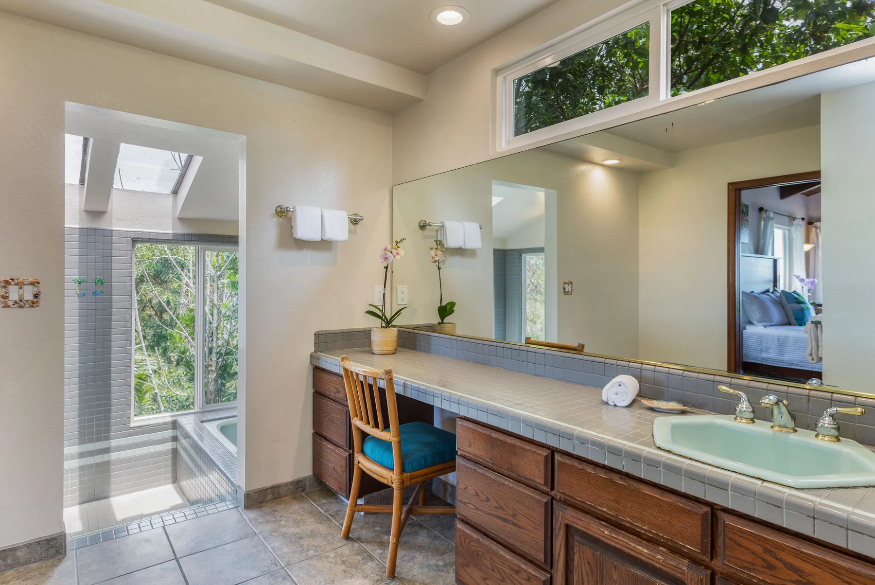 A bathroom vanity with a wide mirror and a chair beside the sink.