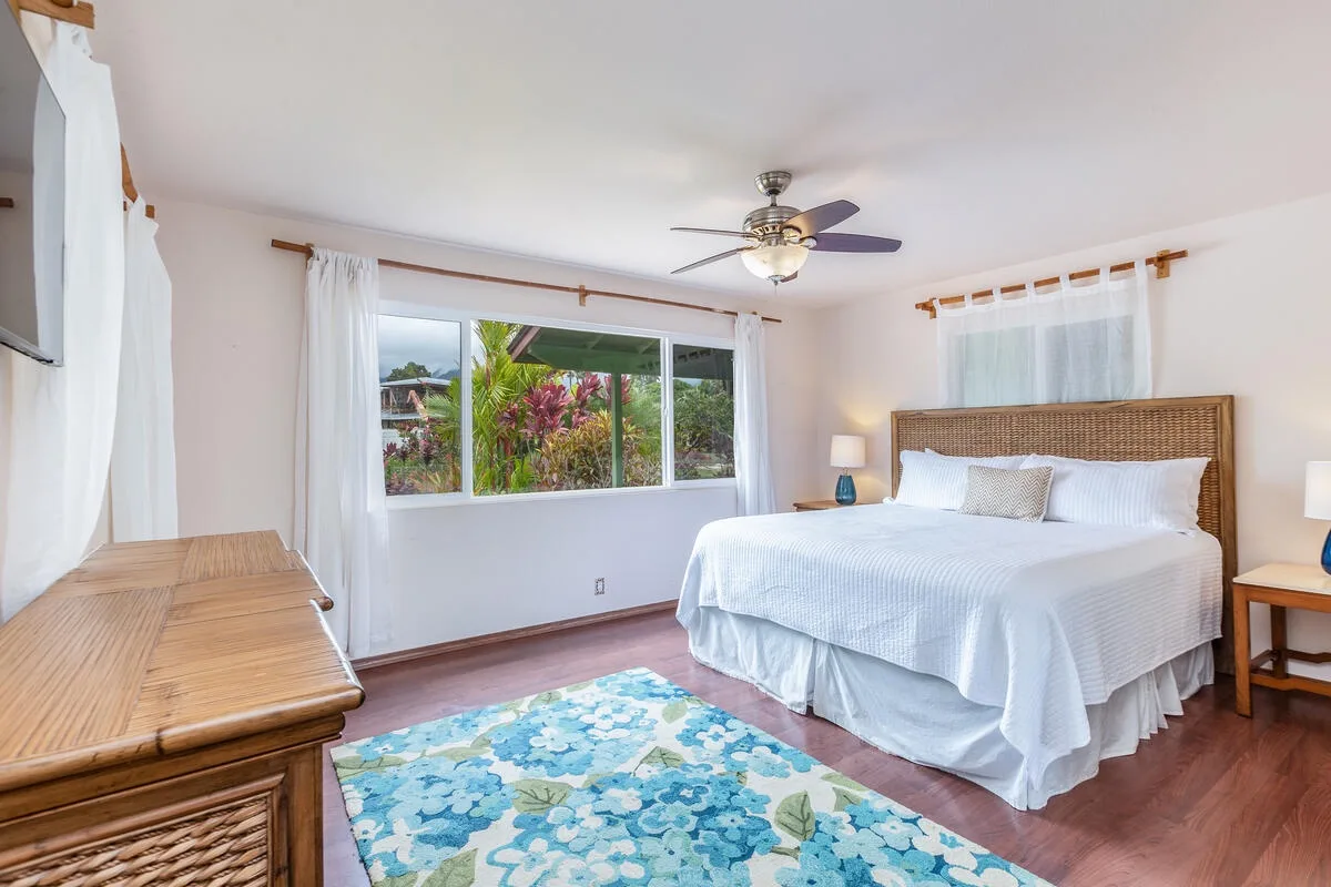 A bright bedroom with a bed, a large window, and a patterned rug.