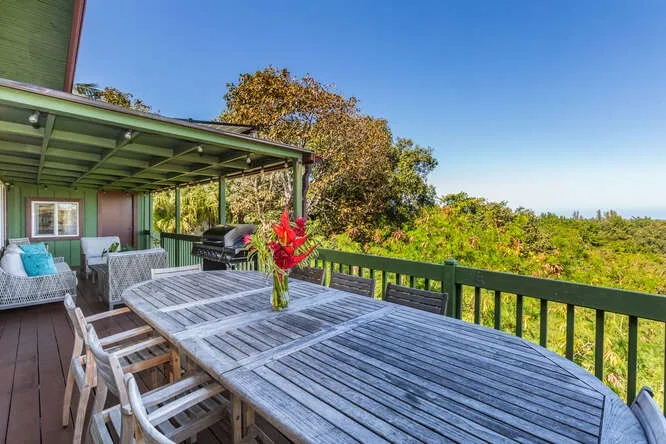 A covered outdoor dining area with a long table overlooking green trees.