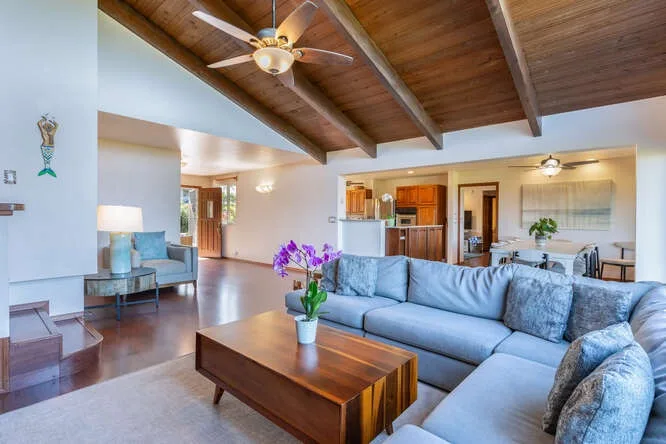 A spacious living room with blue seating beneath a wood-paneled ceiling.