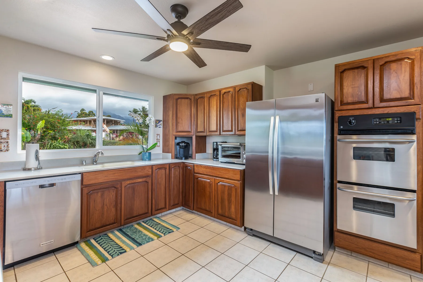 A kitchen with wooden cabinets, stainless steel appliances, and a window overlooking greenery.