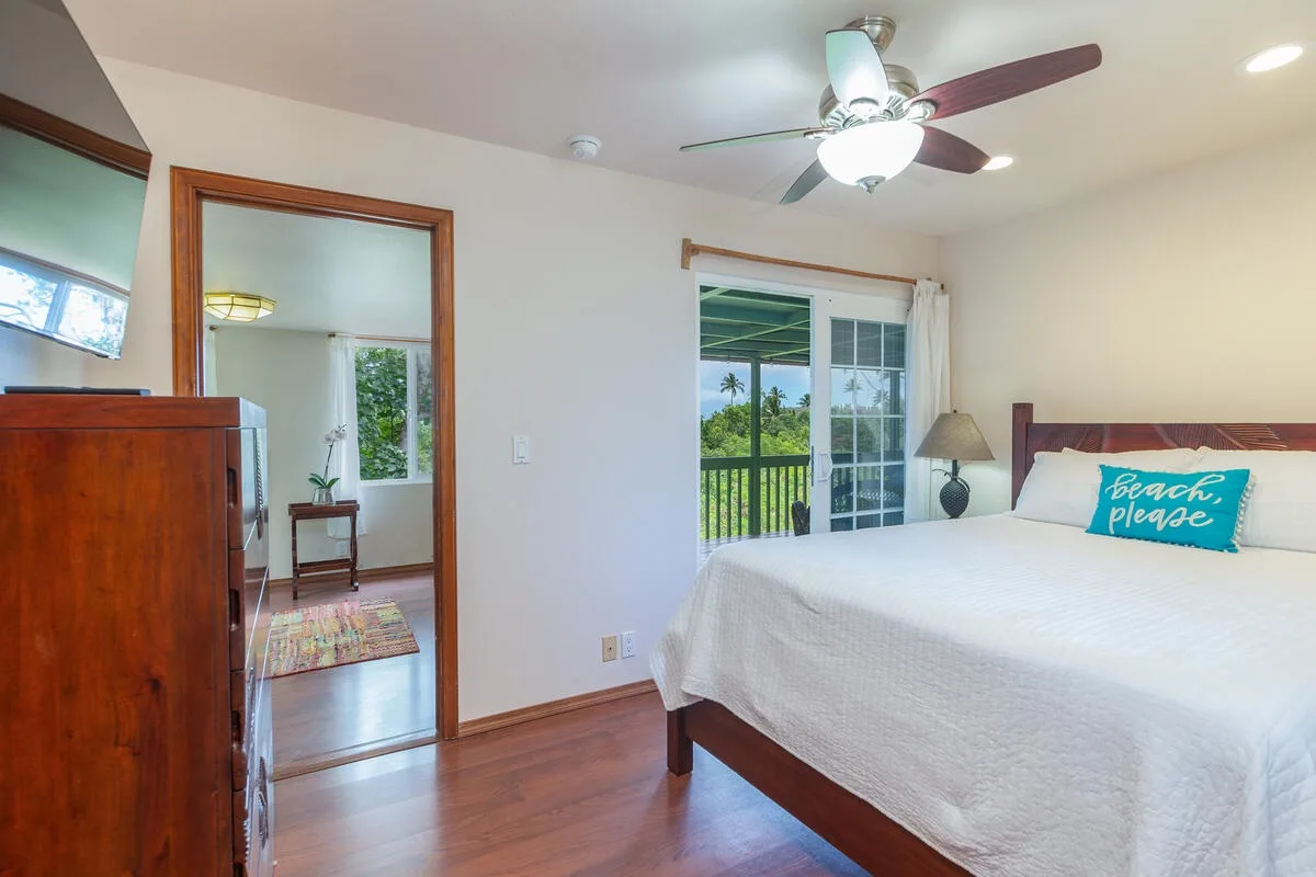 A bedroom with a large bed beside sliding glass doors overlooking greenery.