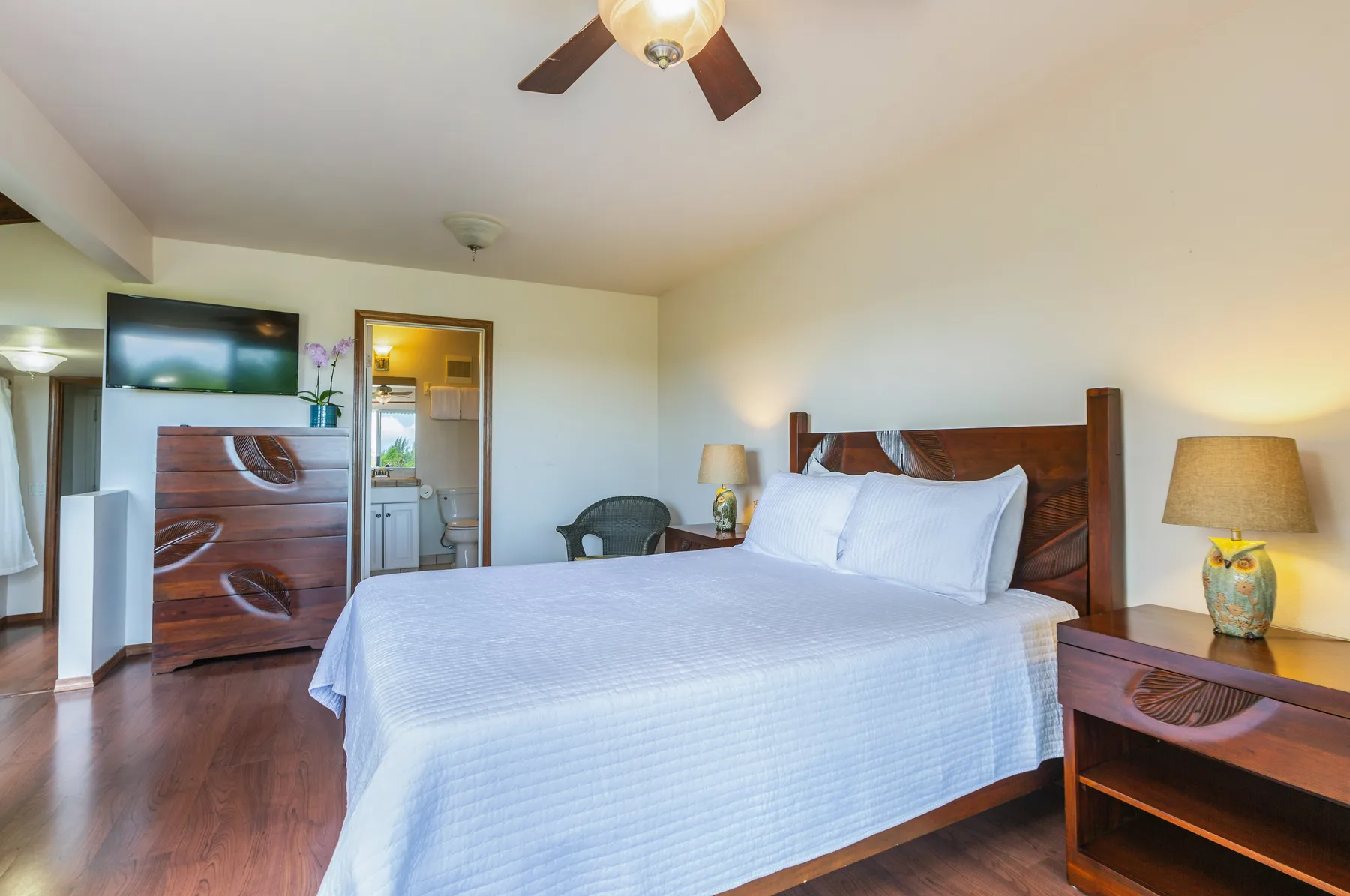A bedroom with a bed, wooden furniture, and a ceiling fan.