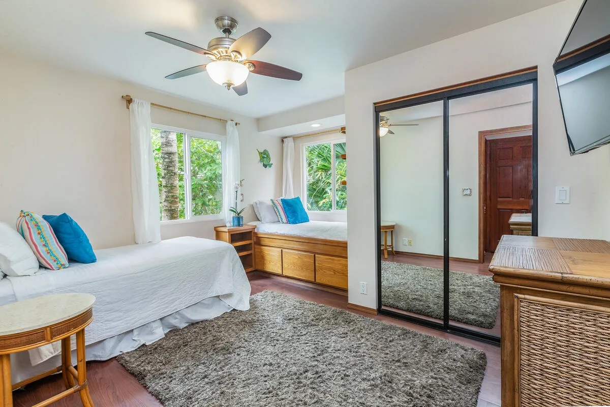 A bright bedroom with beds, windows, and mirrored closet doors.