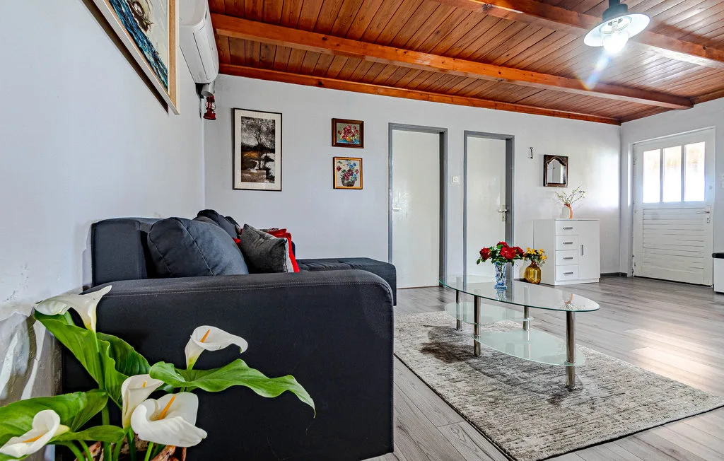 Una sala de estar con asientos oscuros, una mesa de centro de vidrio y cuadros en la pared.