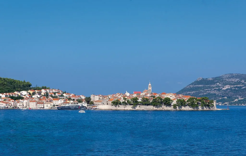 Un pueblo costero con edificios de tejados rojos se extiende junto al mar azul.