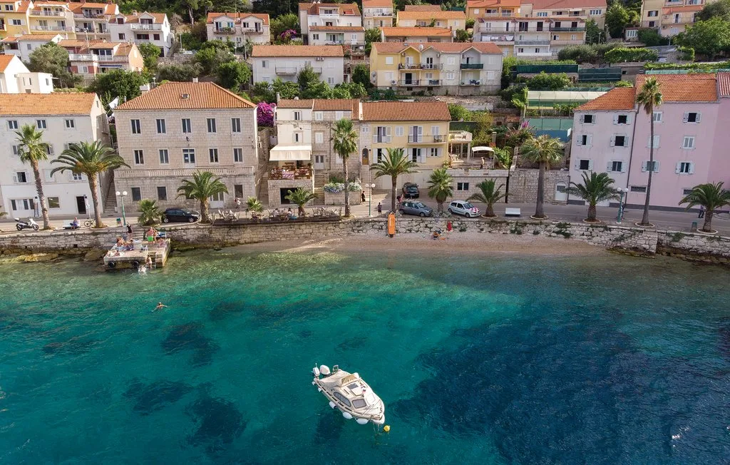 Un pueblo costero bordea una bahía turquesa y clara, con una pequeña embarcación mar adentro.