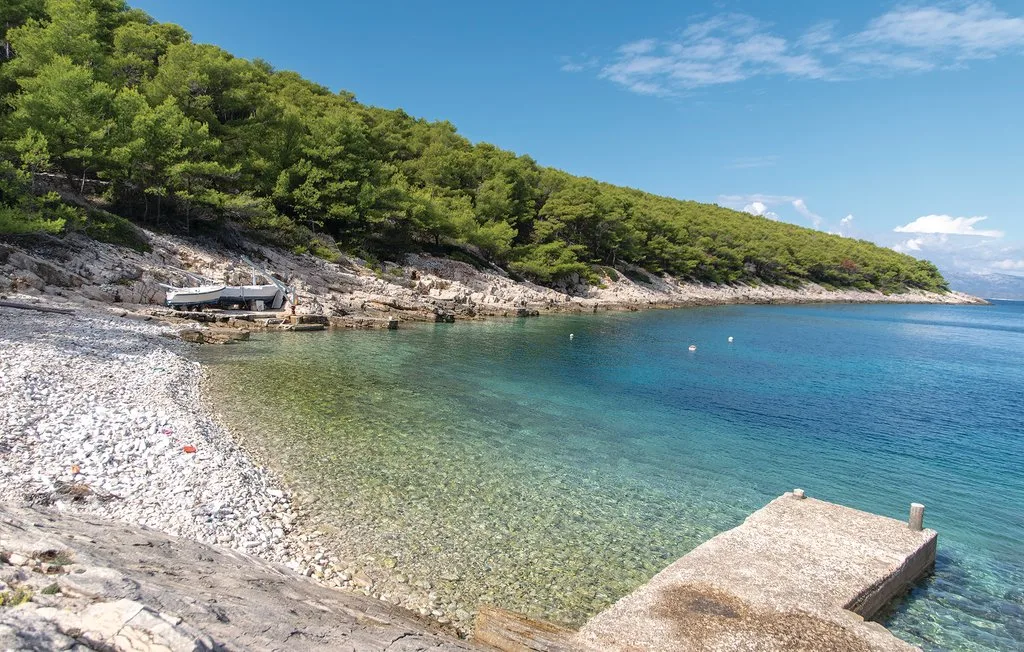 Una bahía de aguas claras con orilla de guijarros y ladera arbolada.