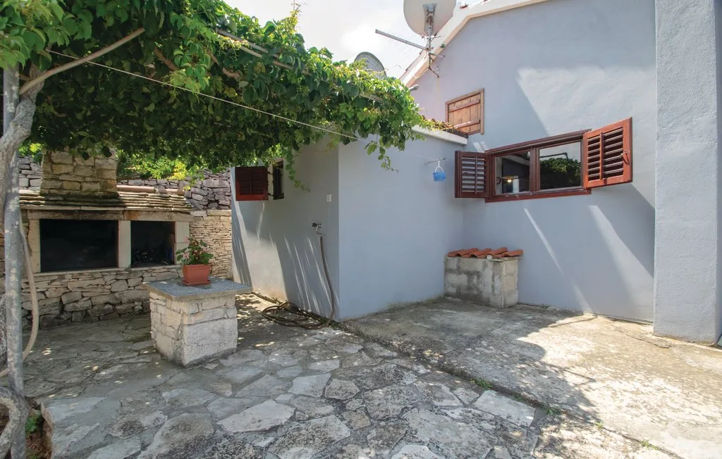 Un patio de piedra con una pérgola frondosa y una pequeña chimenea exterior.