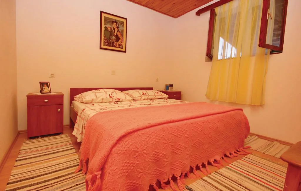 Un dormitorio con una cama cubierta por una manta coral y una ventana con cortinas amarillas.