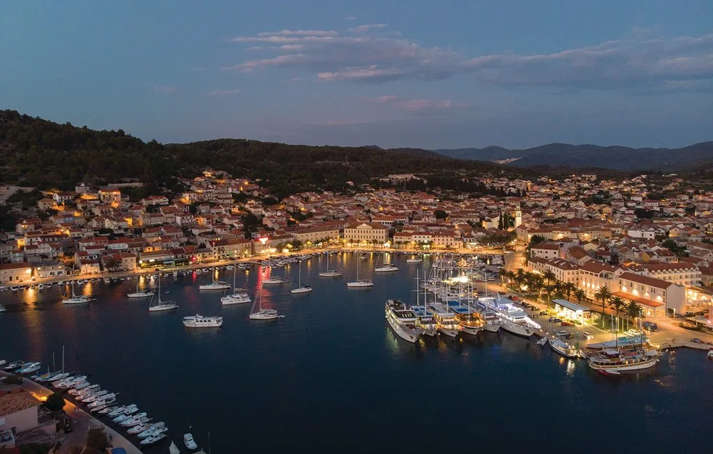 Un puerto costero al anochecer, con embarcaciones en el agua y edificios junto a la costa.