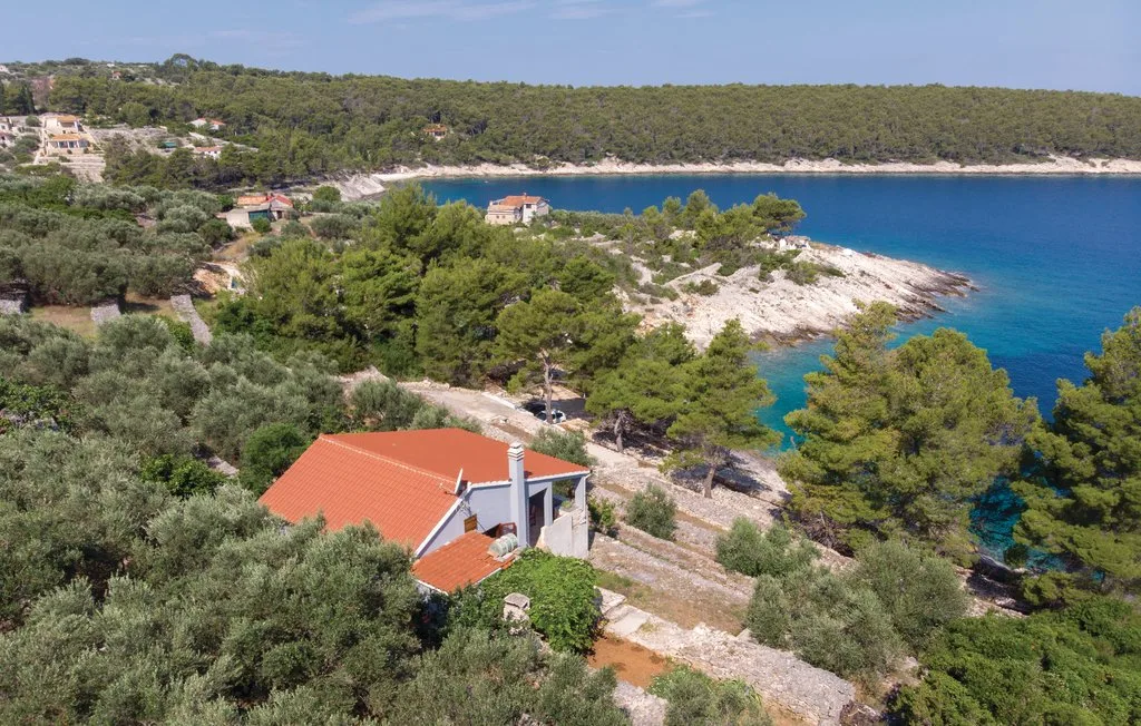 Una casa de techo rojo está entre árboles sobre una costa rocosa y aguas azules.